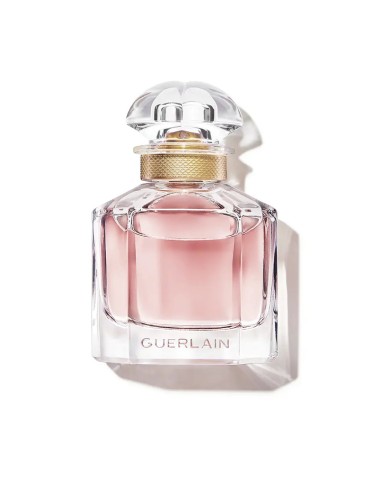 Frasco de perfume de cristal transparente Mon Guerlain con líquido rosa y detalles dorados en el cuello.