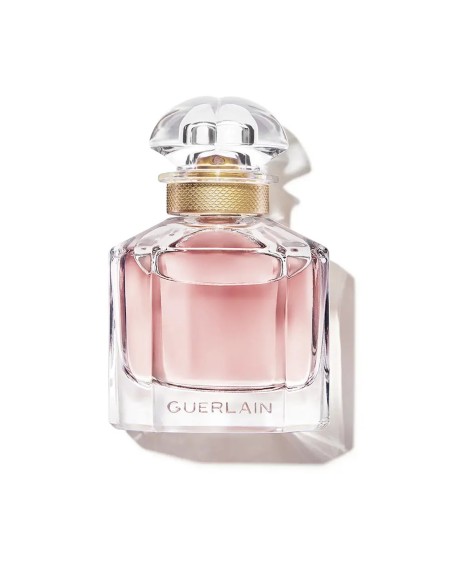 Frasco de perfume de cristal transparente Mon Guerlain con líquido rosa y detalles dorados en el cuello.